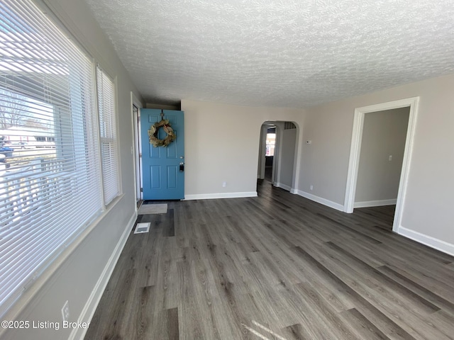 spare room featuring visible vents, baseboards, dark wood finished floors, arched walkways, and a textured ceiling