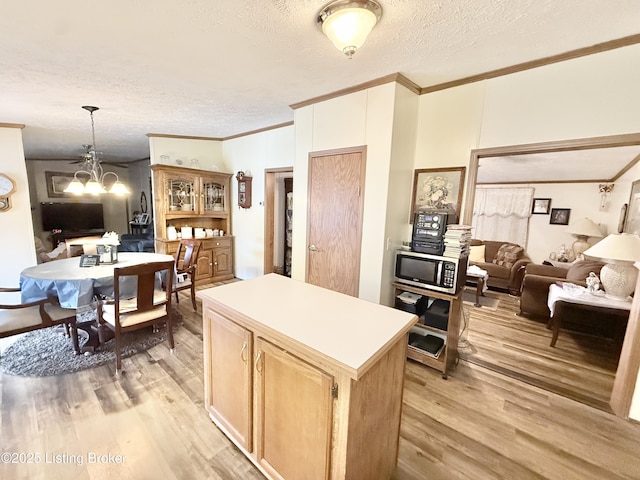 kitchen with light wood finished floors, stainless steel microwave, a center island, crown molding, and open floor plan