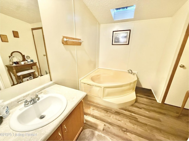 bathroom featuring a textured ceiling, wood finished floors, a skylight, a bath, and vanity