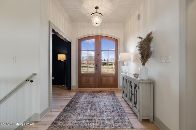 entryway featuring baseboards, light wood finished floors, arched walkways, french doors, and a chandelier