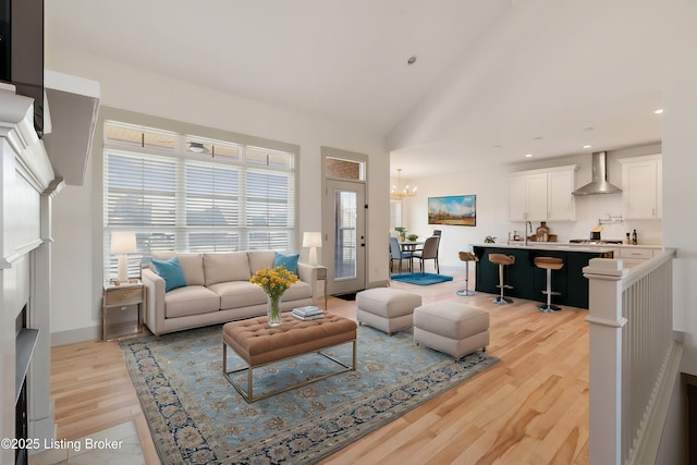 living area featuring baseboards, light wood-type flooring, recessed lighting, a notable chandelier, and high vaulted ceiling