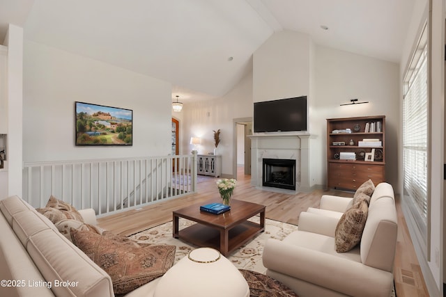 living area featuring high vaulted ceiling, light wood-type flooring, and a premium fireplace