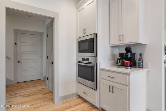 kitchen with light wood-style flooring, built in microwave, oven, light countertops, and white cabinets