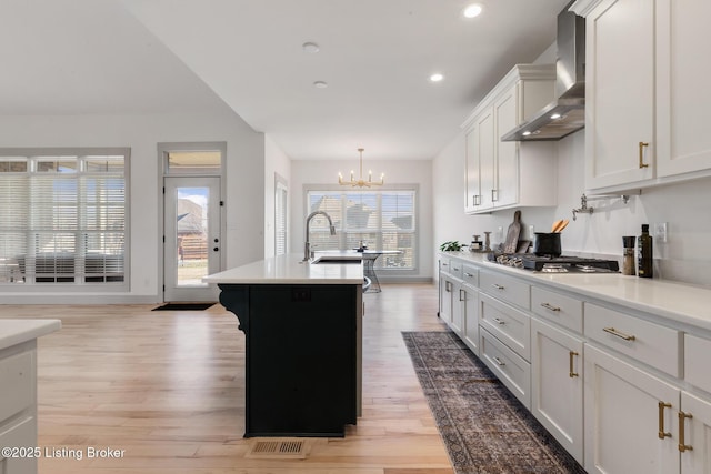 kitchen featuring light countertops, light wood-style flooring, stainless steel gas stovetop, wall chimney exhaust hood, and a sink