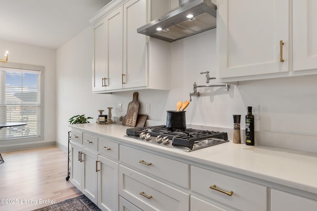 kitchen with white cabinetry, range hood, light countertops, and stainless steel gas cooktop