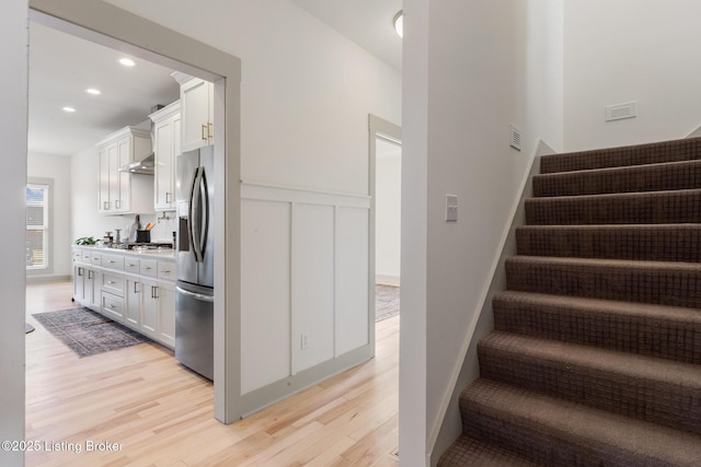 stairs featuring a decorative wall, recessed lighting, wood finished floors, and wainscoting