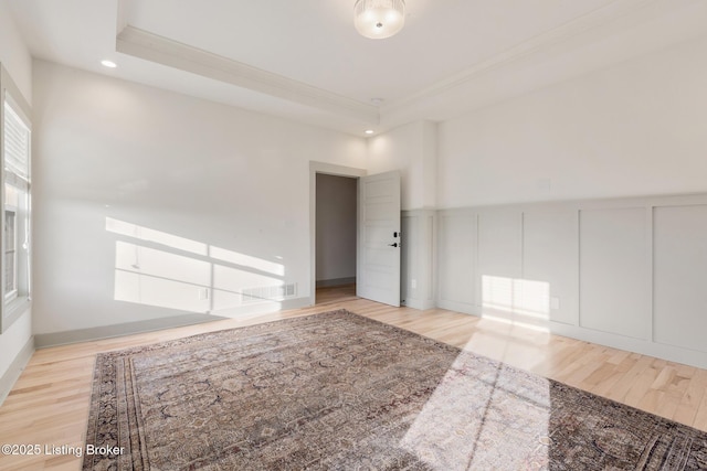 unfurnished room featuring visible vents, a raised ceiling, wood finished floors, and a decorative wall