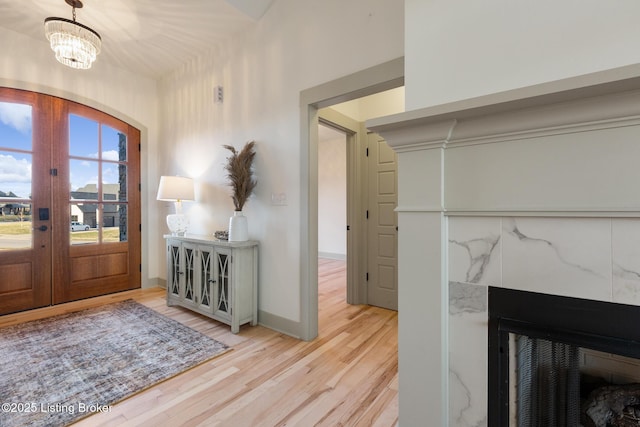 foyer featuring a tiled fireplace, wood finished floors, french doors, baseboards, and a chandelier