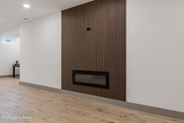 interior details with a glass covered fireplace, recessed lighting, wood finished floors, and baseboards