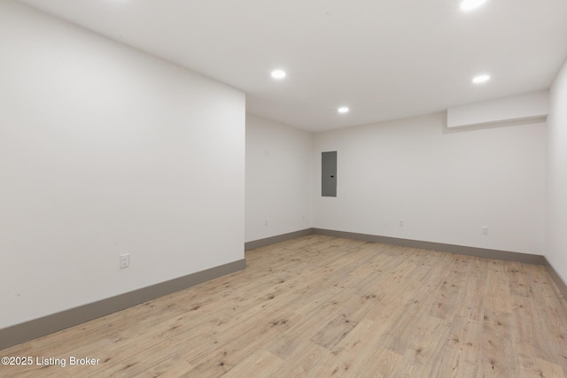 spare room with electric panel, recessed lighting, light wood-type flooring, and baseboards