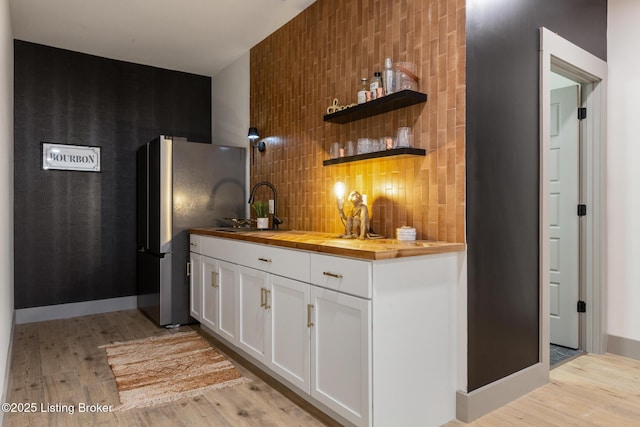 bar with decorative backsplash, light wood-style flooring, freestanding refrigerator, and a sink