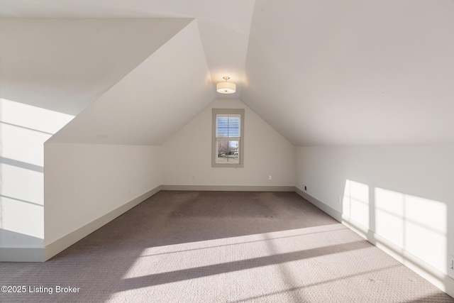 additional living space featuring baseboards, light carpet, and vaulted ceiling