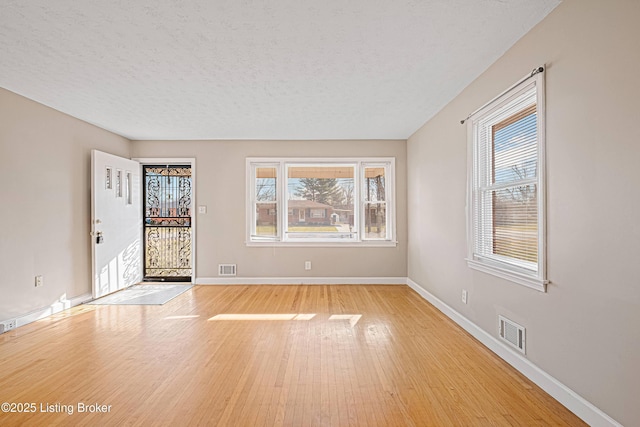 empty room featuring visible vents, a textured ceiling, light wood-type flooring, and baseboards