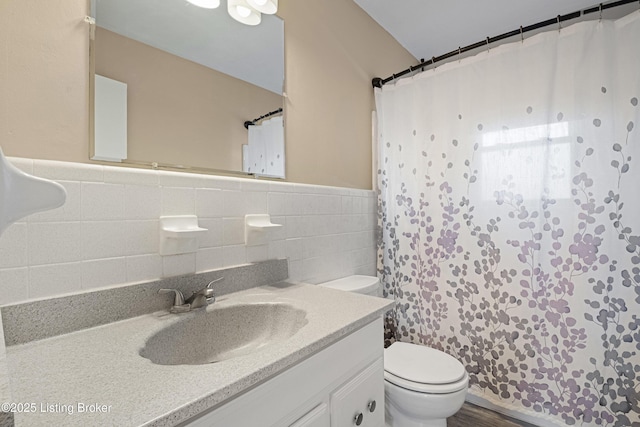 full bath with toilet, a shower with shower curtain, tile walls, wainscoting, and vanity