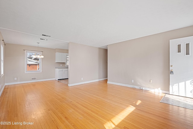 unfurnished living room with visible vents, light wood-style flooring, baseboards, and an inviting chandelier