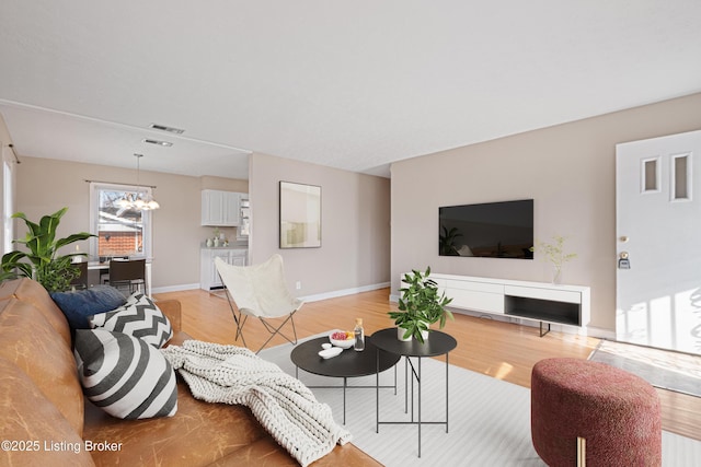 living room with light wood-style flooring, a notable chandelier, visible vents, and baseboards