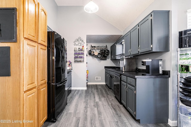 kitchen featuring dark countertops, baseboards, vaulted ceiling, freestanding refrigerator, and wood finished floors