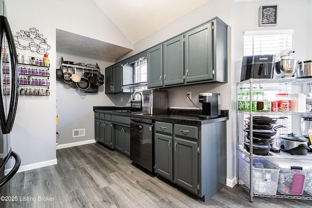 kitchen featuring dark countertops, visible vents, vaulted ceiling, dishwashing machine, and wood finished floors