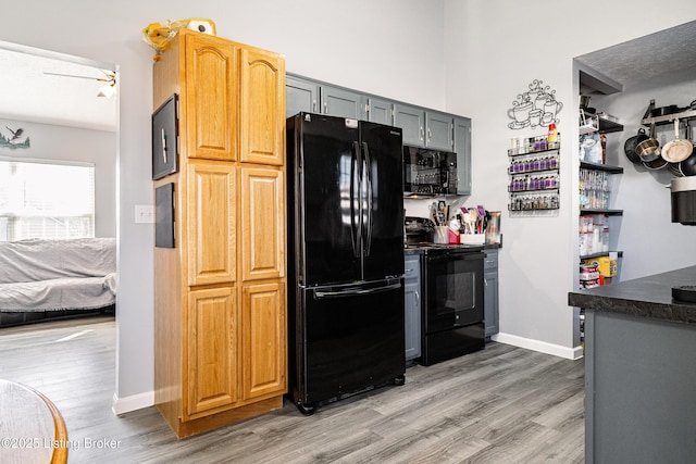 kitchen featuring light wood-type flooring, black appliances, dark countertops, a textured ceiling, and baseboards