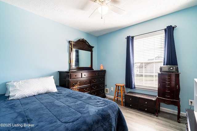 bedroom with ceiling fan, wood finished floors, baseboards, and a textured ceiling