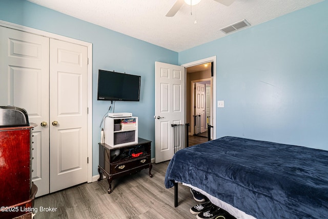 bedroom featuring ceiling fan, visible vents, a textured ceiling, and wood finished floors