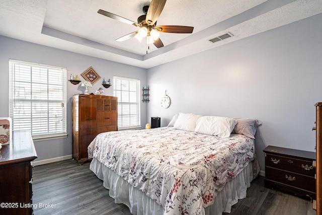 bedroom with a tray ceiling, baseboards, visible vents, and wood finished floors