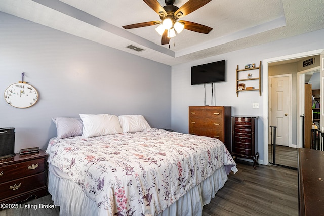 bedroom with visible vents, a raised ceiling, a textured ceiling, and dark wood-style floors