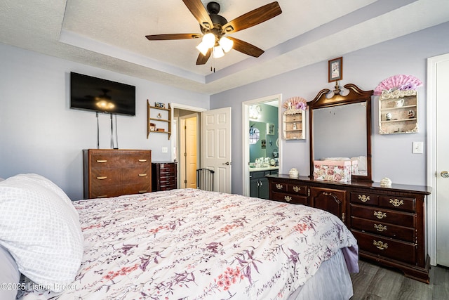 bedroom with dark wood-type flooring, a tray ceiling, a textured ceiling, ensuite bath, and ceiling fan