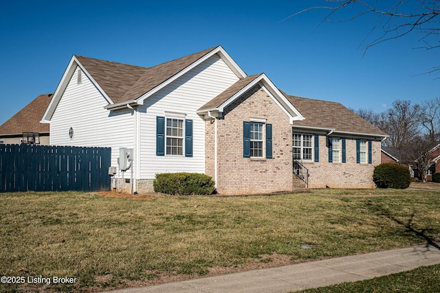 view of side of home with brick siding, roof with shingles, a yard, and fence