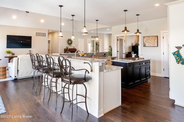 kitchen featuring visible vents, dark wood-type flooring, a kitchen breakfast bar, recessed lighting, and a large island with sink