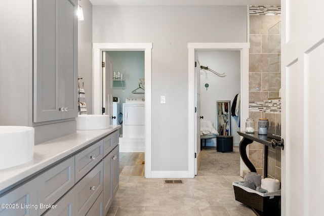 full bathroom featuring baseboards, visible vents, double vanity, a sink, and independent washer and dryer