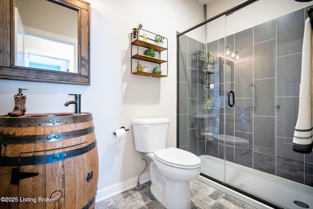 full bathroom featuring toilet, a stall shower, stone finish floor, baseboards, and vanity