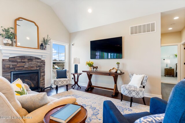 living room featuring visible vents, wood finished floors, a stone fireplace, baseboards, and vaulted ceiling