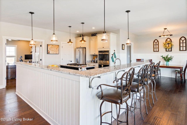 kitchen with a large island, appliances with stainless steel finishes, dark wood-type flooring, and light stone counters