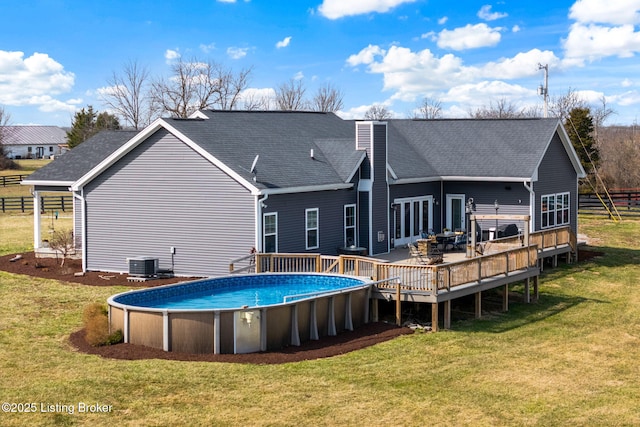 rear view of property with central air condition unit, a wooden deck, roof with shingles, a yard, and an outdoor pool