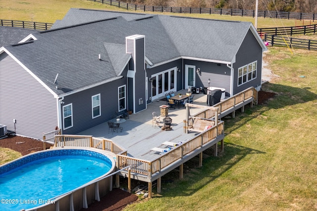 rear view of property featuring a deck, outdoor dining space, fence, a yard, and a shingled roof