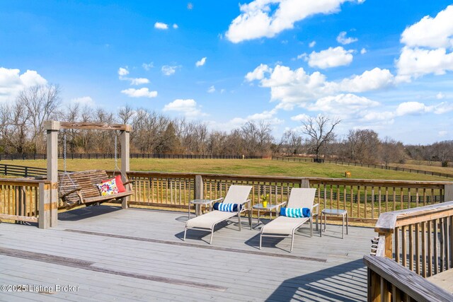 wooden terrace with a rural view, fence, and a lawn