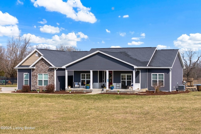 view of front facade featuring stone siding, covered porch, a front lawn, and central AC