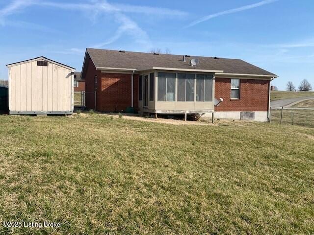 back of house with brick siding, fence, a lawn, a sunroom, and an outbuilding