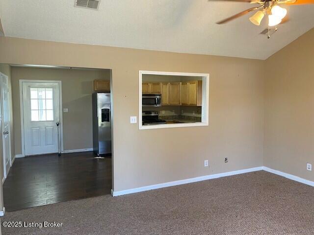 unfurnished room featuring visible vents, lofted ceiling, dark colored carpet, baseboards, and ceiling fan