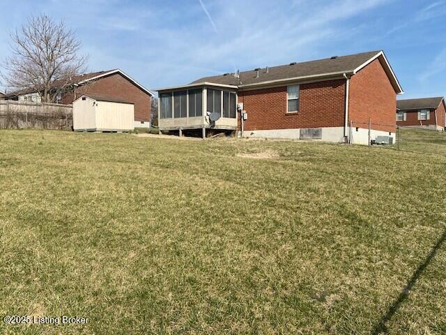 back of property with brick siding, an outdoor structure, a yard, and a sunroom