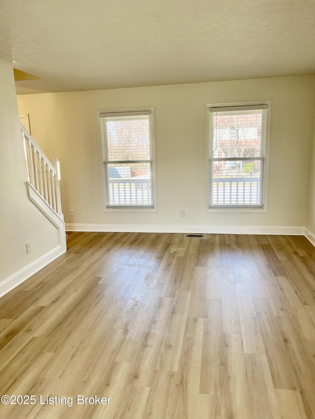 empty room featuring stairway, baseboards, visible vents, and wood finished floors