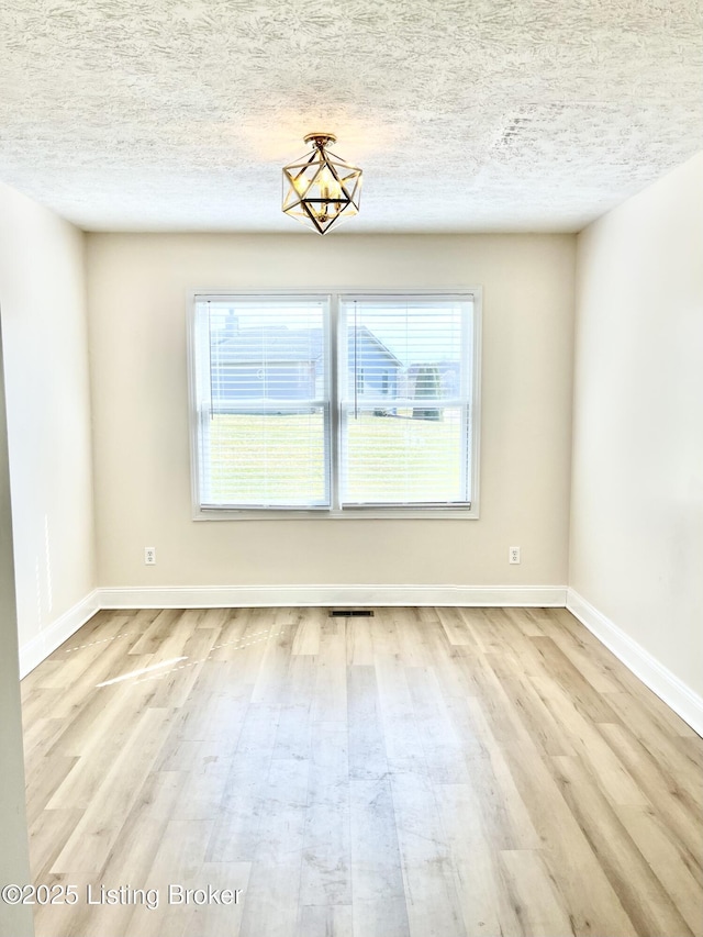 empty room featuring visible vents, wood finished floors, baseboards, and a textured ceiling