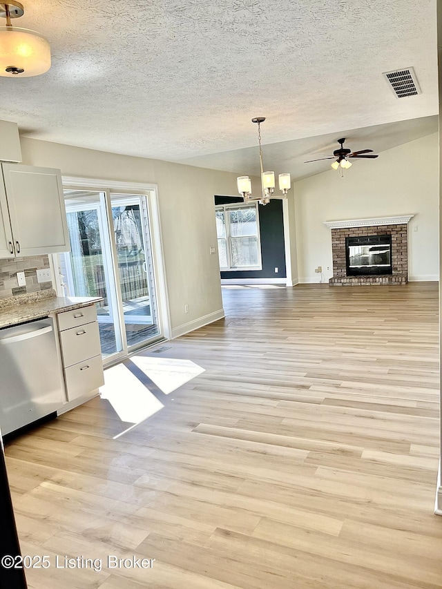 interior space featuring light wood-type flooring, visible vents, stainless steel dishwasher, white cabinetry, and a brick fireplace