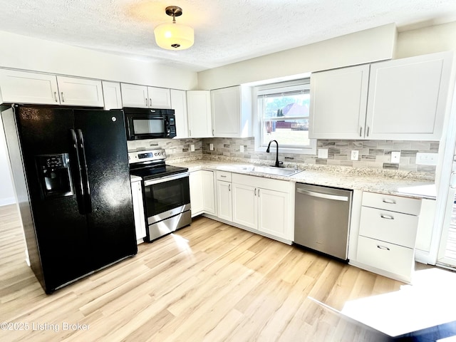 kitchen with light wood finished floors, tasteful backsplash, white cabinets, black appliances, and a sink