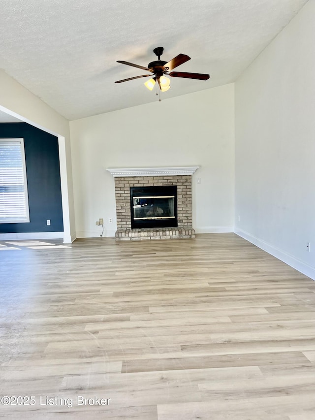 unfurnished living room with a brick fireplace, baseboards, vaulted ceiling, wood finished floors, and a textured ceiling