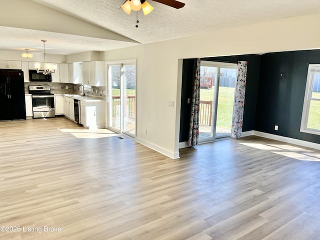 unfurnished living room featuring vaulted ceiling, light wood-style flooring, a healthy amount of sunlight, and a sink