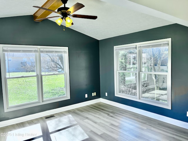 empty room with a wealth of natural light, visible vents, lofted ceiling with beams, and baseboards