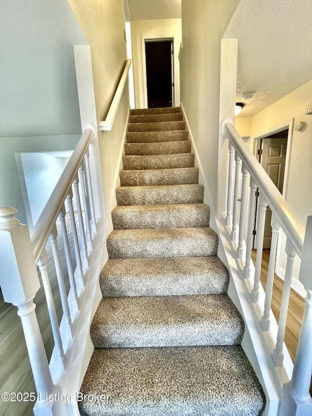 stairs featuring baseboards, a textured ceiling, and wood finished floors