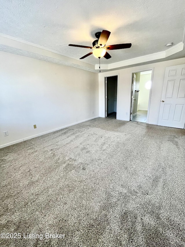 unfurnished bedroom featuring ensuite bathroom, a ceiling fan, a tray ceiling, a textured ceiling, and baseboards